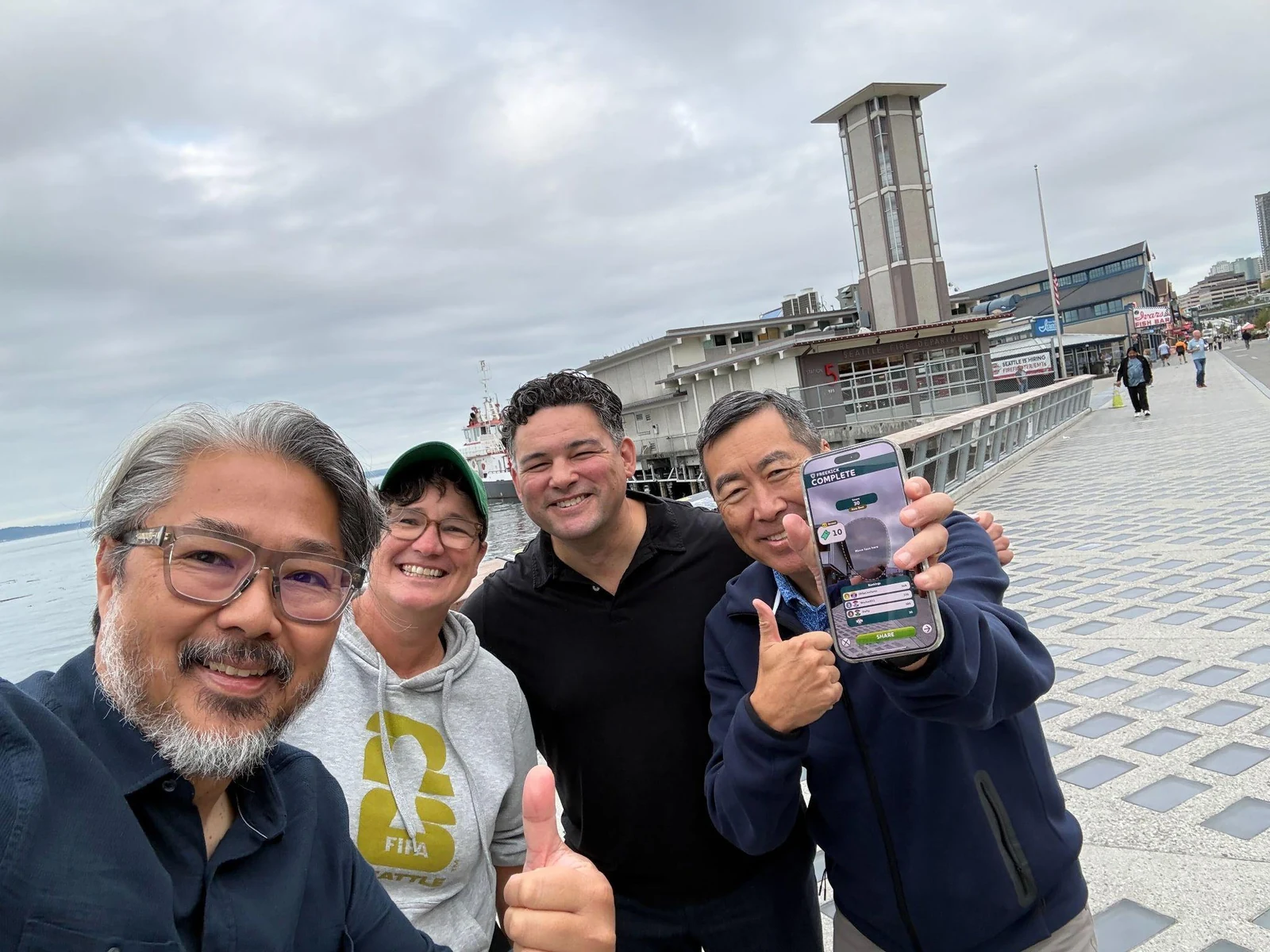 Four people on Seattle's waterfront, with one displaying the SEA&WIN app on a phone
